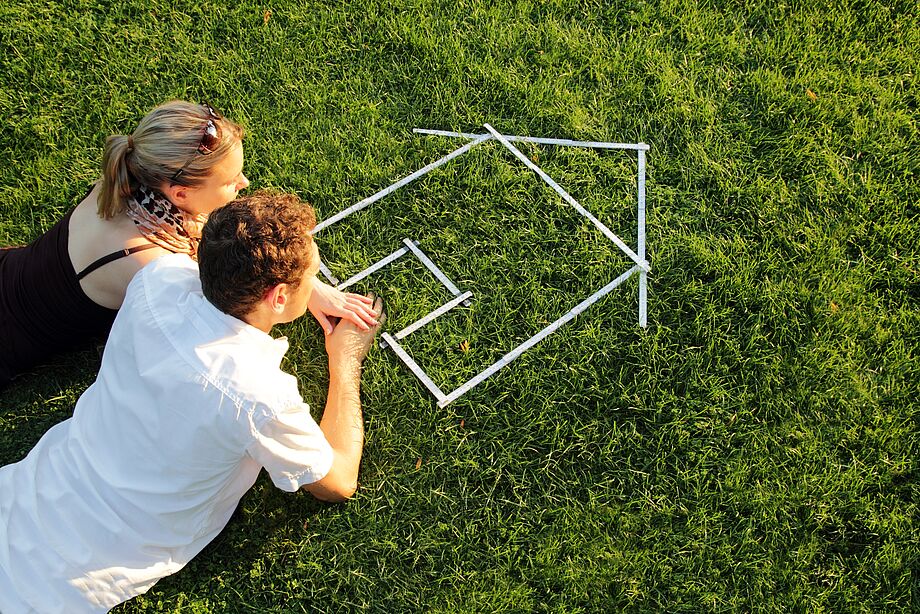 Paar auf Gras liegend mit aus Maßbändern zusammengesetztem Haus.