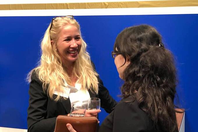 Zwei Frauen in Anzug reden mit Sekt in den Händen.